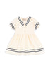 A sailor-inspired white dress with navy stripes on the collar and sleeves, and a soft silhouette. The dress is made from organic cotton and has a GOTS certification.