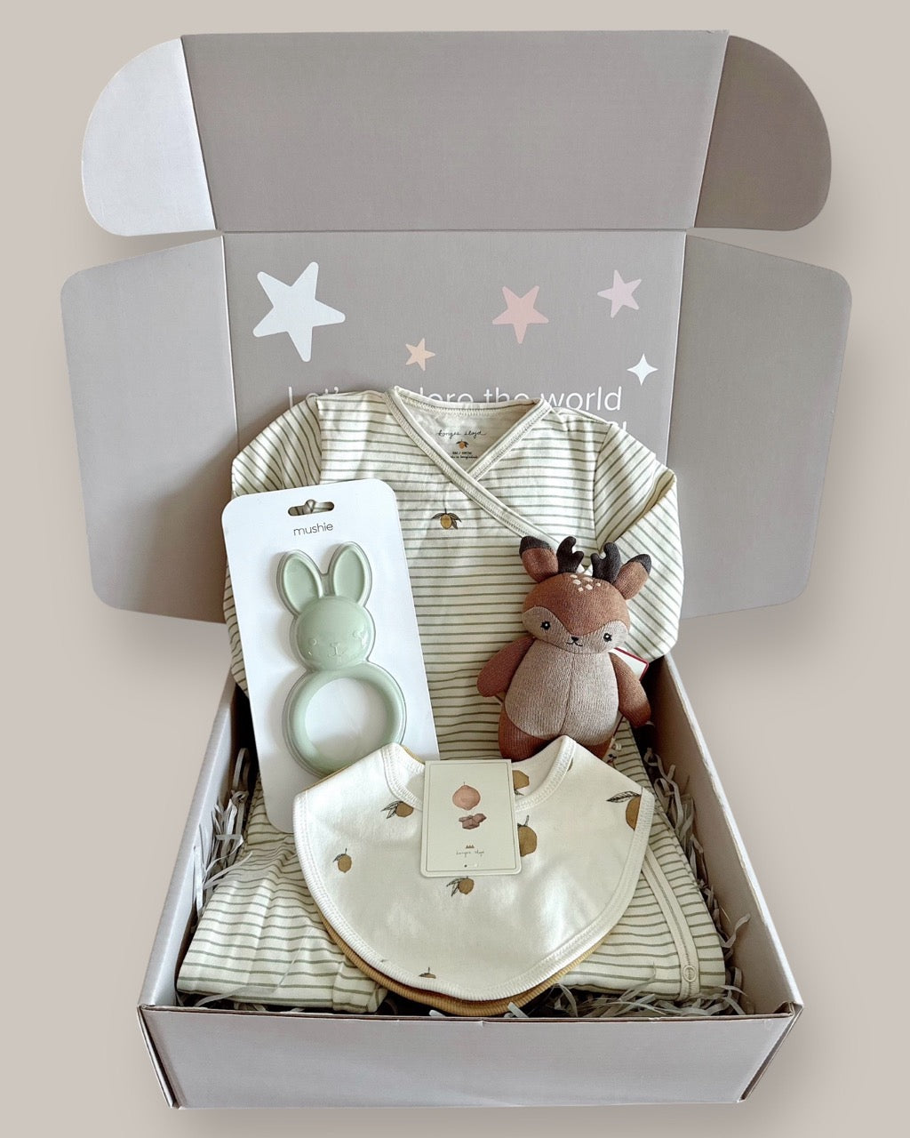 Baby gift set with clothing, teether, and plush toy in a box on a light background