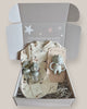 Baby gift set with items including a bottle, bib, and rattle in a box with a message card.