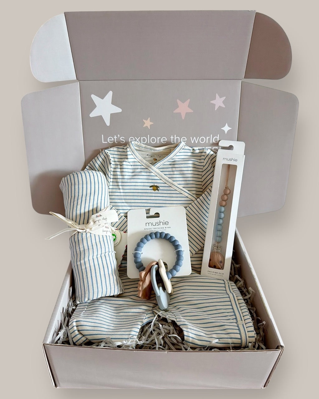 Baby gift set with striped outfit, blanket, and toys in a box on a light background