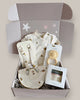 Baby product set including a bib, teether, and other items in a box on a light background