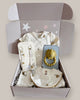 Baby gift set with clothes, teether, and accessories in a box on a light background