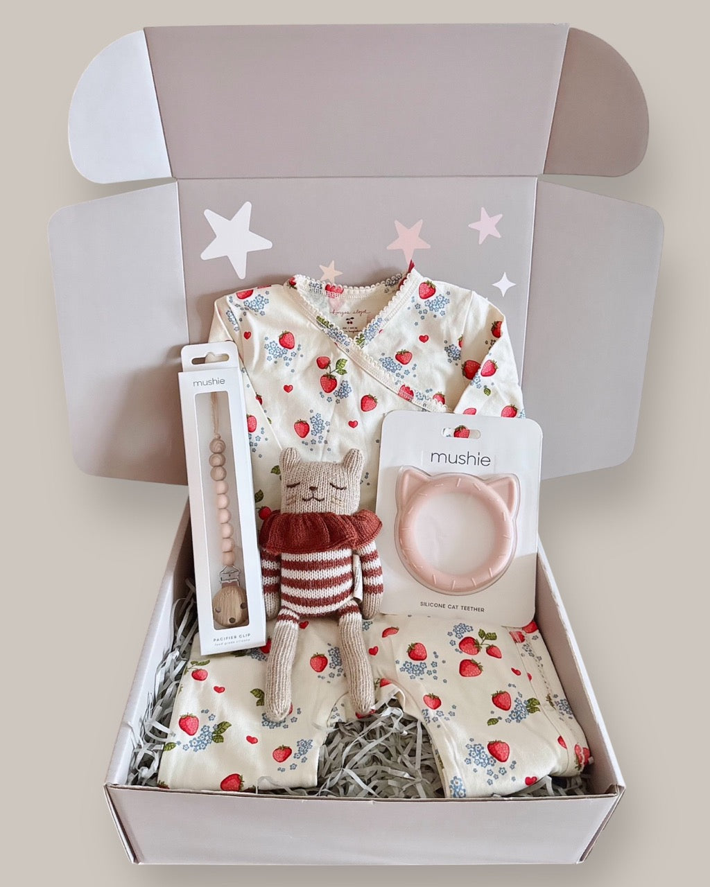 Baby gift set with baby clothes, a toy, and a headband in a box on a light background