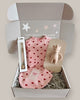 Baby gift set with pink outfit, booties, and toy in a box on a light background