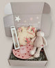 Baby gift set with clothes, socks, and a plush toy in a box on a light background