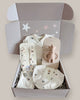 Baby gift set with clothes, bib, and rattle in a box on a light background