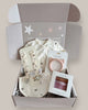 Baby gift set with clothes, teether, and other items in a box on a light background
